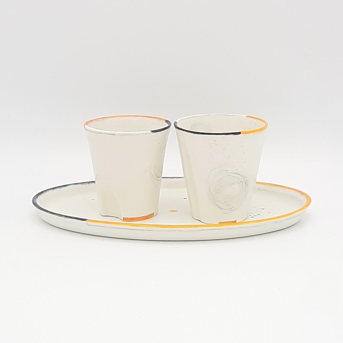 Kaolin - Guðný Magnúsdóttir - The Tea glasses or Espresso cups have each their own character in form and decoration. They are in white porcelain, hand painted individually  with orange and black lines on the edge and come in a set of two.